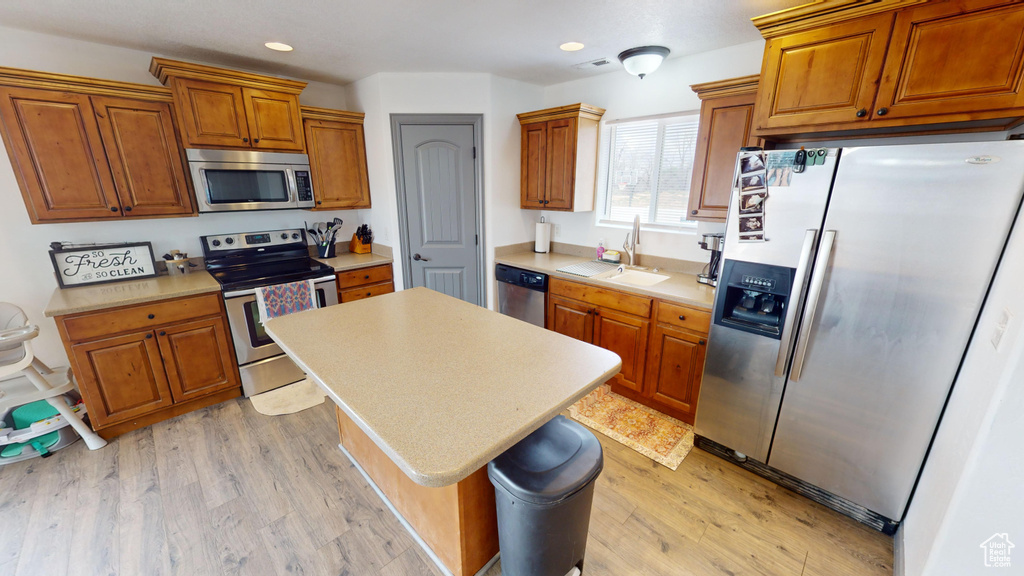 Kitchen with sink, light wood-type flooring, appliances with stainless steel finishes, and a kitchen island