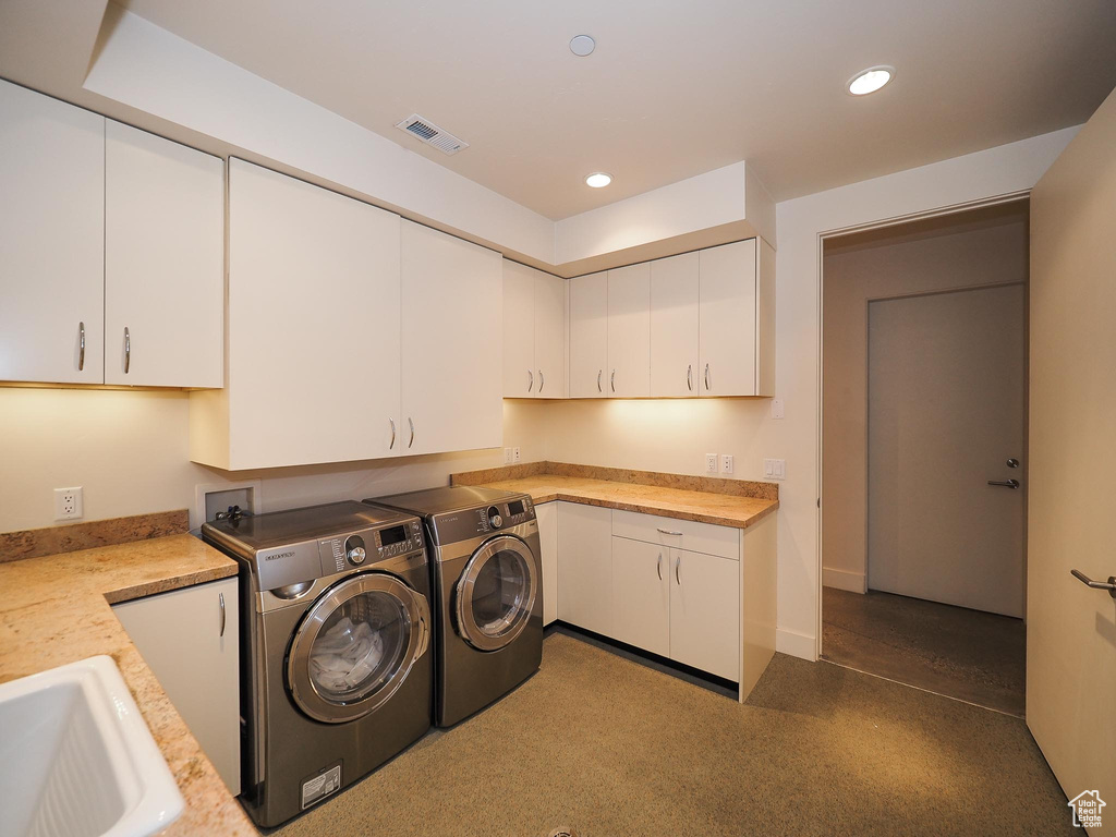 Washroom with sink, washing machine and dryer, and cabinets