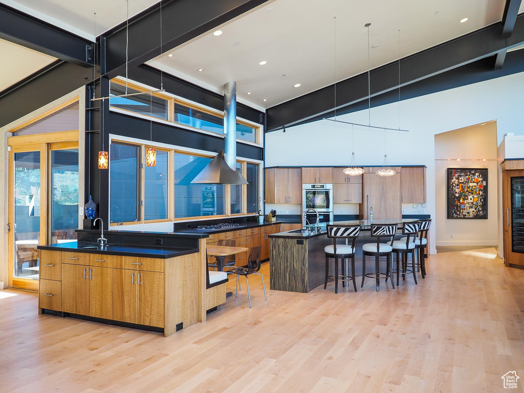 Kitchen with a breakfast bar, a center island, a high ceiling, light wood-type flooring, and double oven