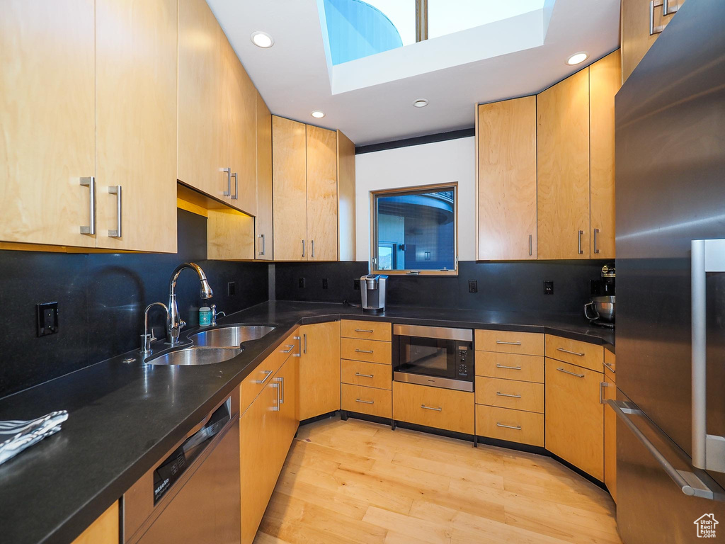 Kitchen with decorative backsplash, black microwave, a skylight, light wood-type flooring, and stainless steel fridge