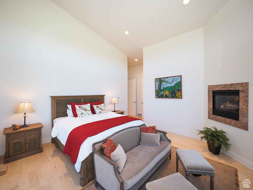 Bedroom with hardwood / wood-style flooring, high vaulted ceiling, and a premium fireplace