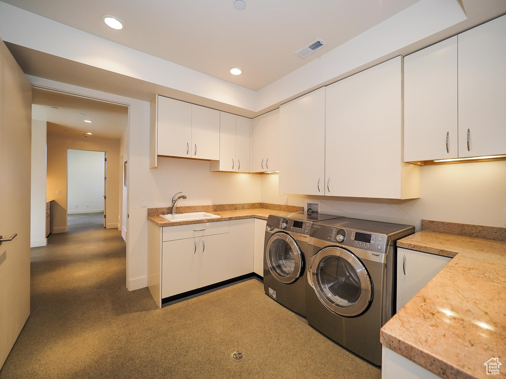 Clothes washing area featuring sink, washing machine and dryer, and cabinets