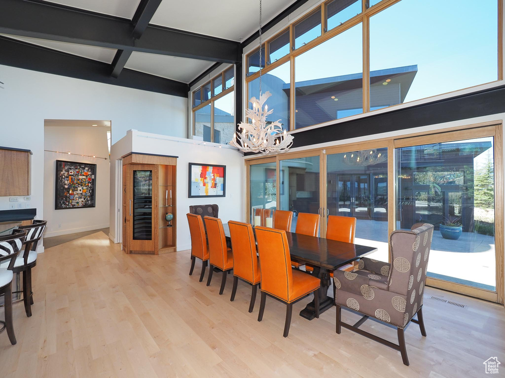 Dining area with a towering ceiling, beamed ceiling, light hardwood / wood-style floors, and a chandelier