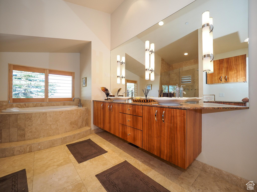 Bathroom featuring dual vanity, a relaxing tiled tub, tile patterned floors, and a healthy amount of sunlight