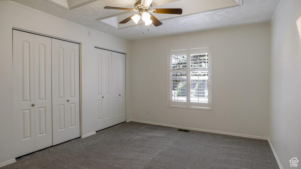 Unfurnished bedroom with carpet flooring, ceiling fan, two closets, and ornamental molding