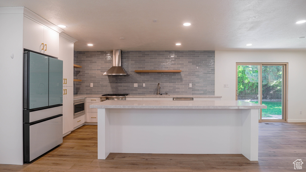 Kitchen featuring appliances with stainless steel finishes, light hardwood / wood-style flooring, wall chimney range hood, and white cabinetry