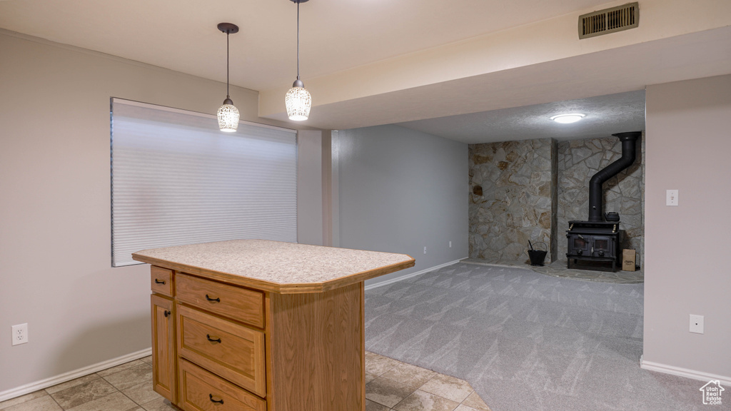 Kitchen featuring light colored carpet, a wood stove, pendant lighting, and a kitchen island