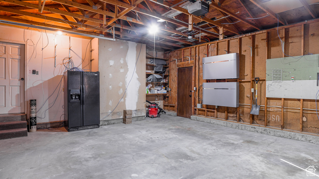 Garage with a garage door opener and black fridge with ice dispenser