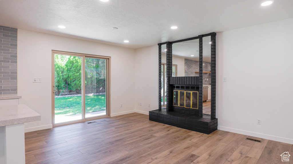 Unfurnished living room with light wood-type flooring, a large fireplace, and brick wall