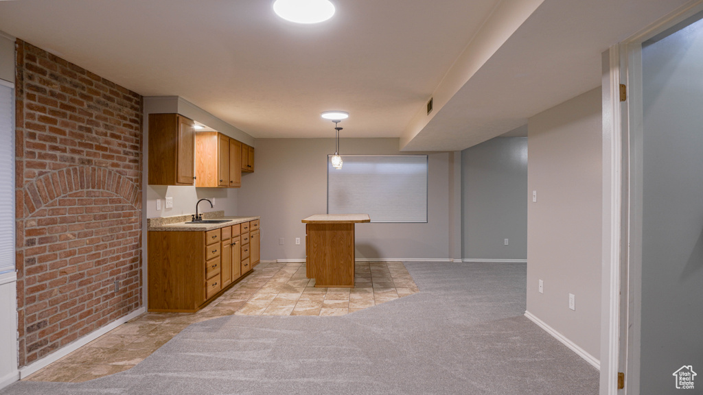 Kitchen with sink, brick wall, light colored carpet, and pendant lighting