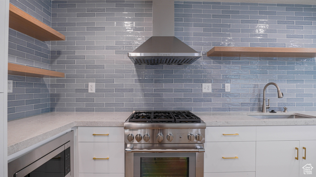 Kitchen featuring appliances with stainless steel finishes, wall chimney range hood, decorative backsplash, and white cabinets