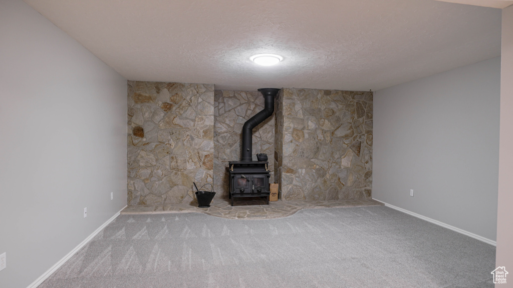 Unfurnished living room featuring a wood stove, a textured ceiling, and carpet flooring