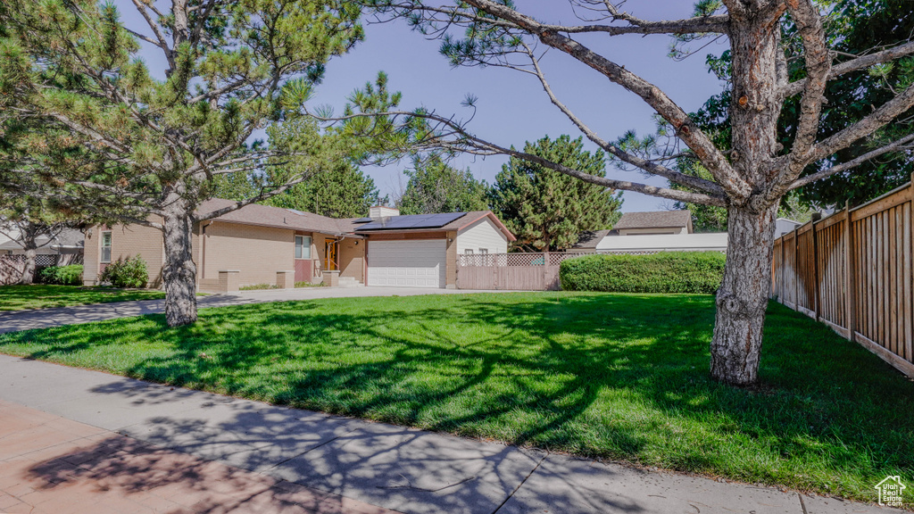 Ranch-style house with a front lawn, solar panels, and a garage