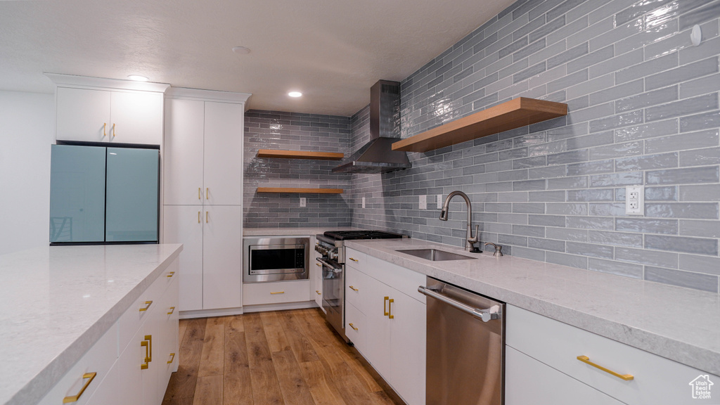 Kitchen with wall chimney range hood, backsplash, white cabinetry, appliances with stainless steel finishes, and sink