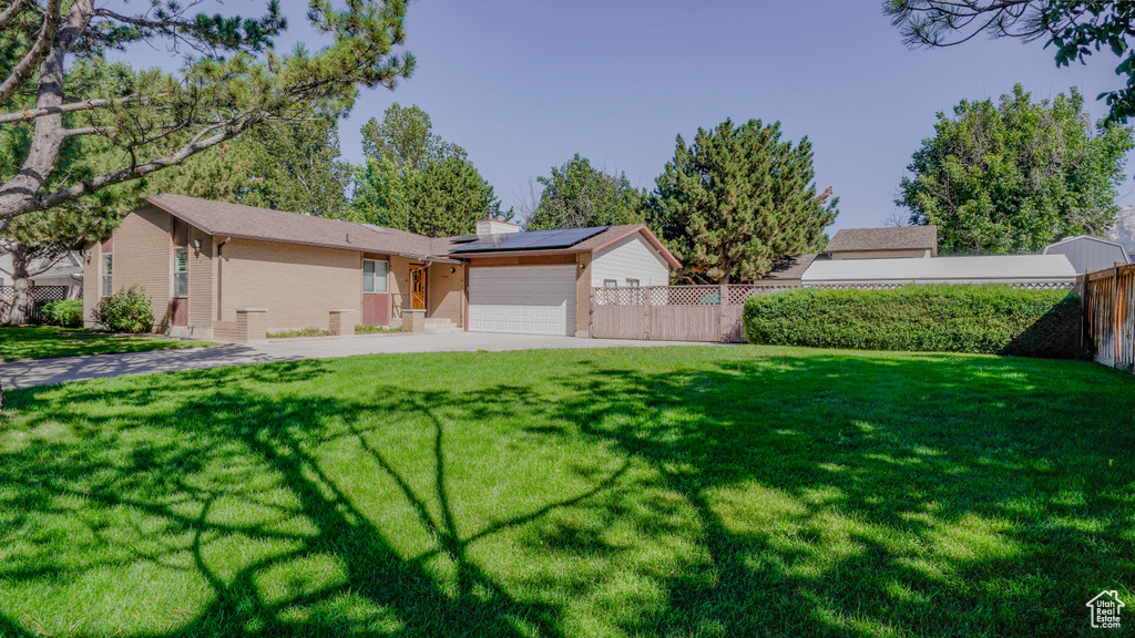 Ranch-style house featuring a front lawn, solar panels, and a garage