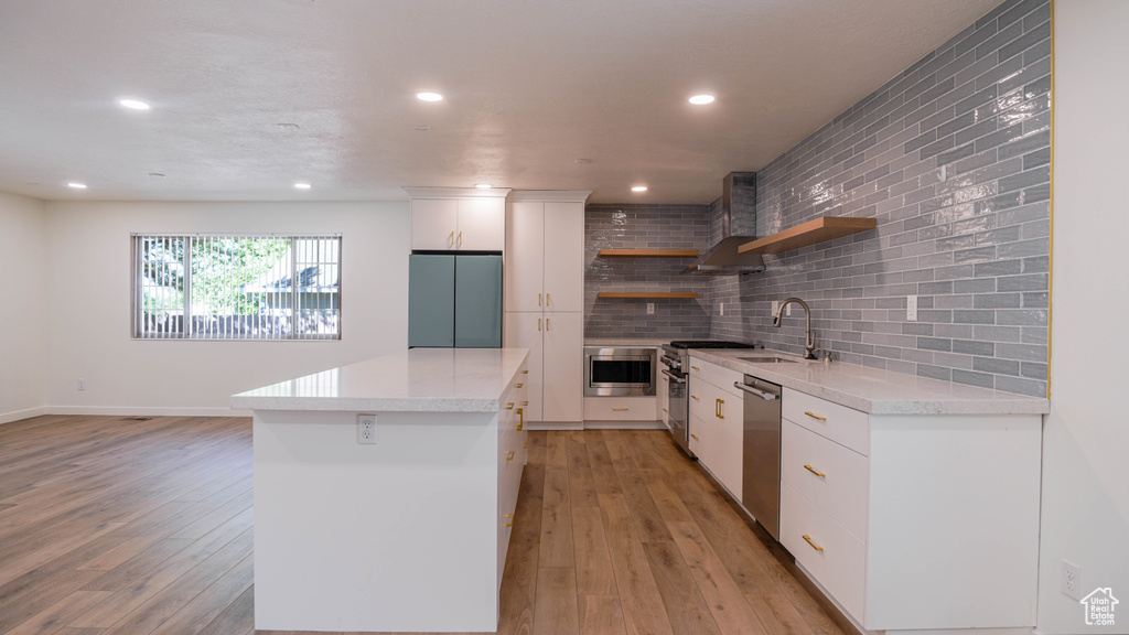 Kitchen featuring decorative backsplash, light hardwood / wood-style floors, stainless steel appliances, wall chimney range hood, and white cabinets