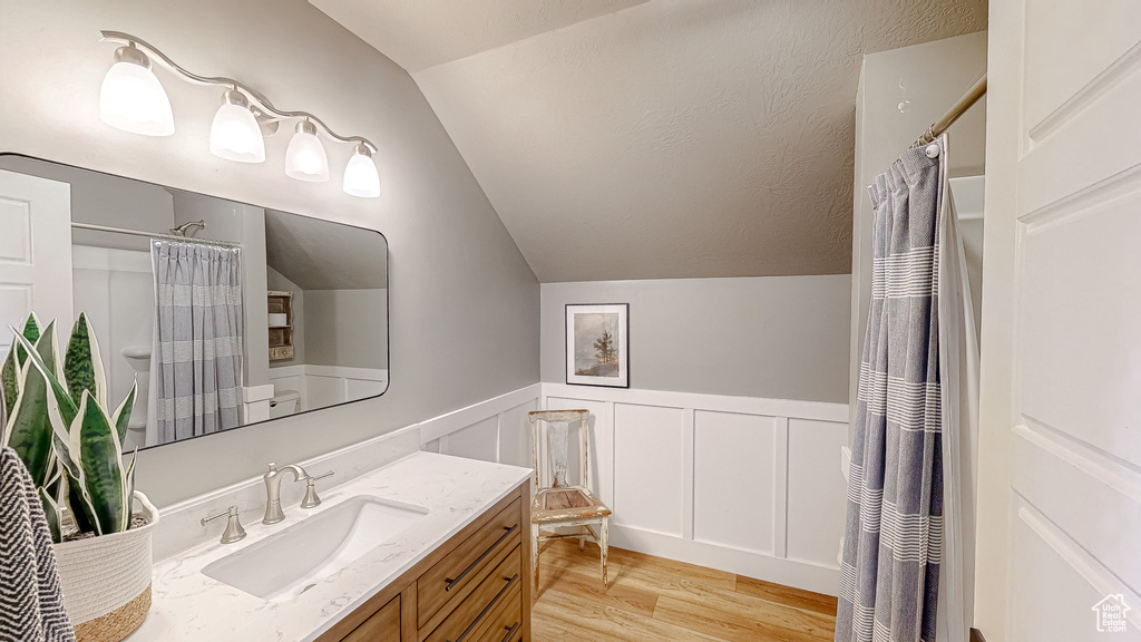 Bathroom with a shower with curtain, vaulted ceiling, vanity, and hardwood / wood-style floors