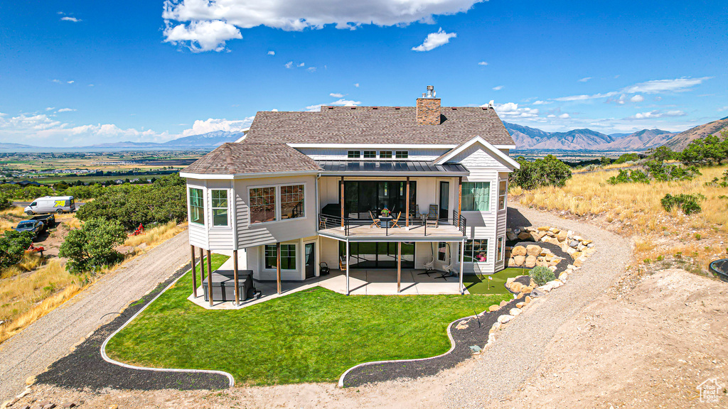 Back of house with a mountain view, a patio, and a yard