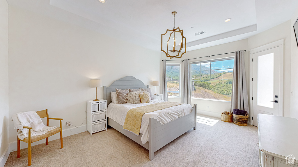 Carpeted bedroom featuring a notable chandelier and a tray ceiling