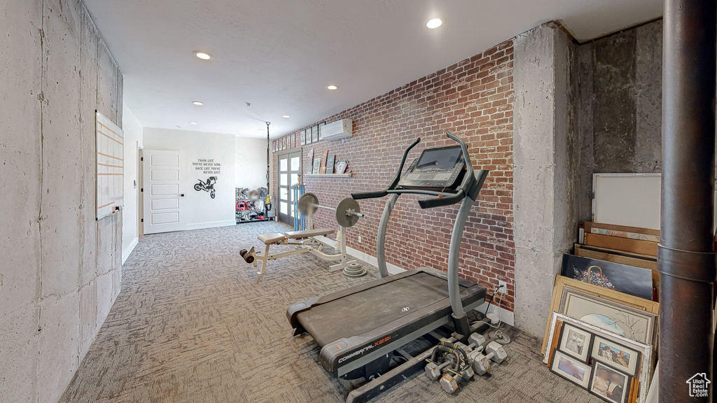 Exercise room with carpet floors, lofted ceiling, brick wall, and a wall mounted AC