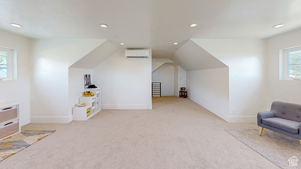 Bonus room with light colored carpet, a wall unit AC, and a healthy amount of sunlight