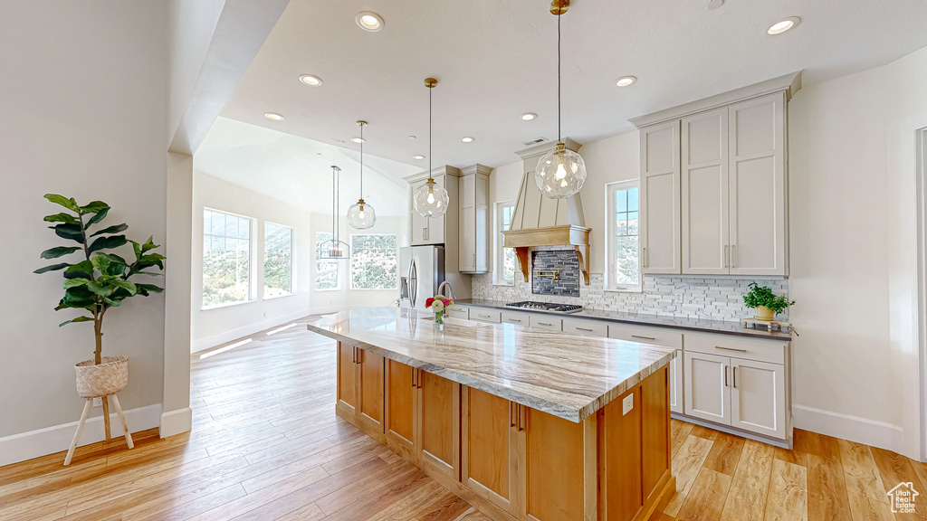 Kitchen featuring custom range hood, light hardwood / wood-style flooring, backsplash, light stone counters, and a center island