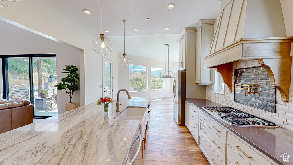 Kitchen with dark stone countertops, decorative light fixtures, light wood-type flooring, appliances with stainless steel finishes, and tasteful backsplash