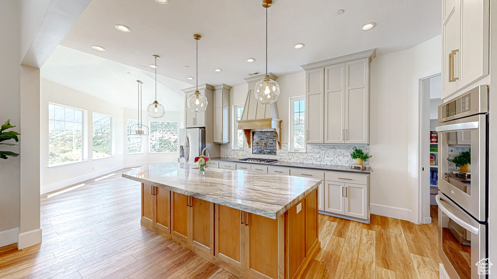 Kitchen featuring appliances with stainless steel finishes, a center island with sink, light hardwood / wood-style floors, and tasteful backsplash