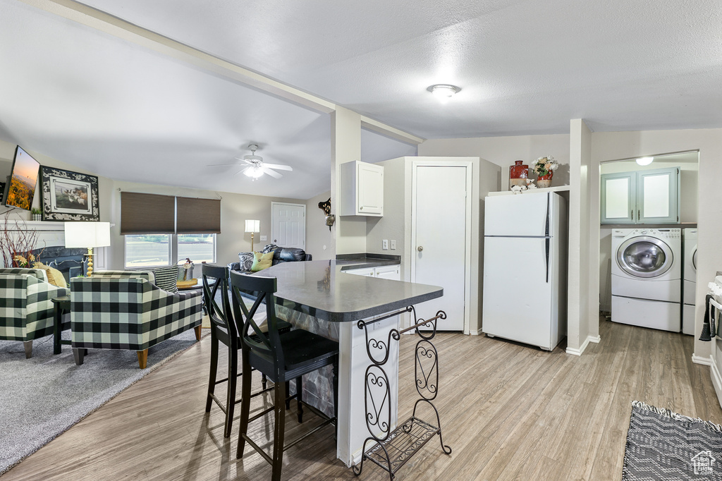 Kitchen with white cabinetry, white fridge, light hardwood / wood-style floors, ceiling fan, and a breakfast bar area