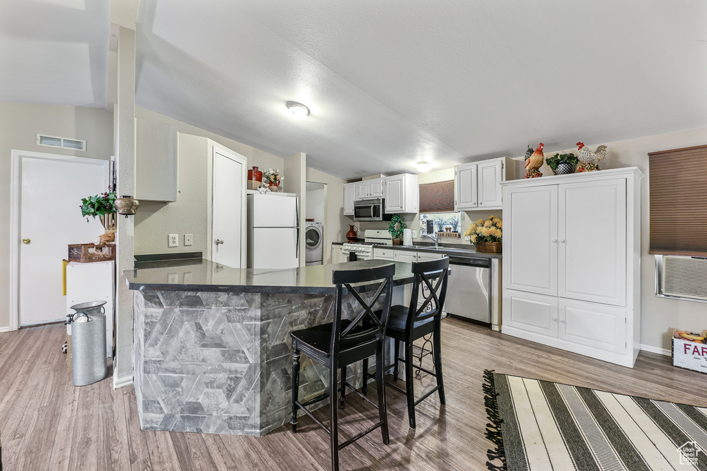 Kitchen with light wood-type flooring, a kitchen breakfast bar, white cabinetry, and stainless steel appliances