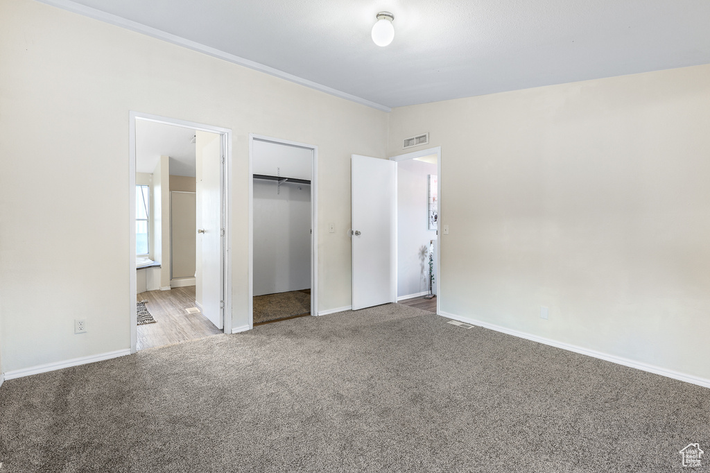 Unfurnished bedroom with light colored carpet, a closet, ensuite bath, and crown molding