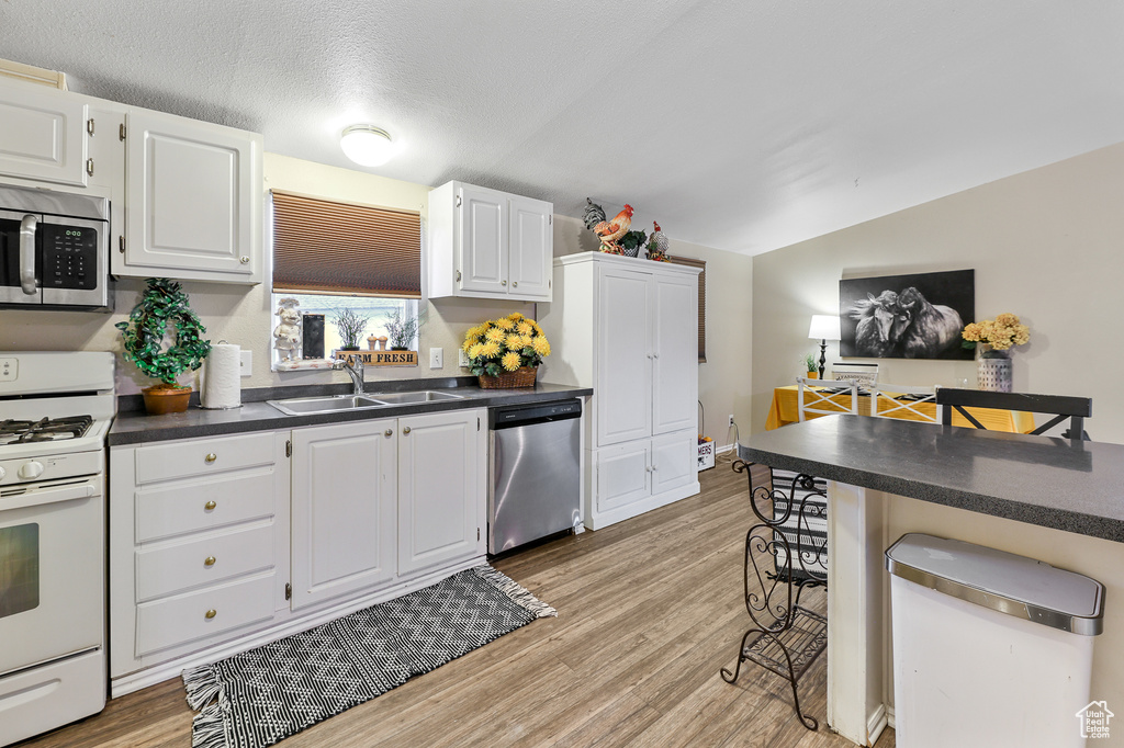 Kitchen with sink, light wood-type flooring, white cabinetry, and appliances with stainless steel finishes