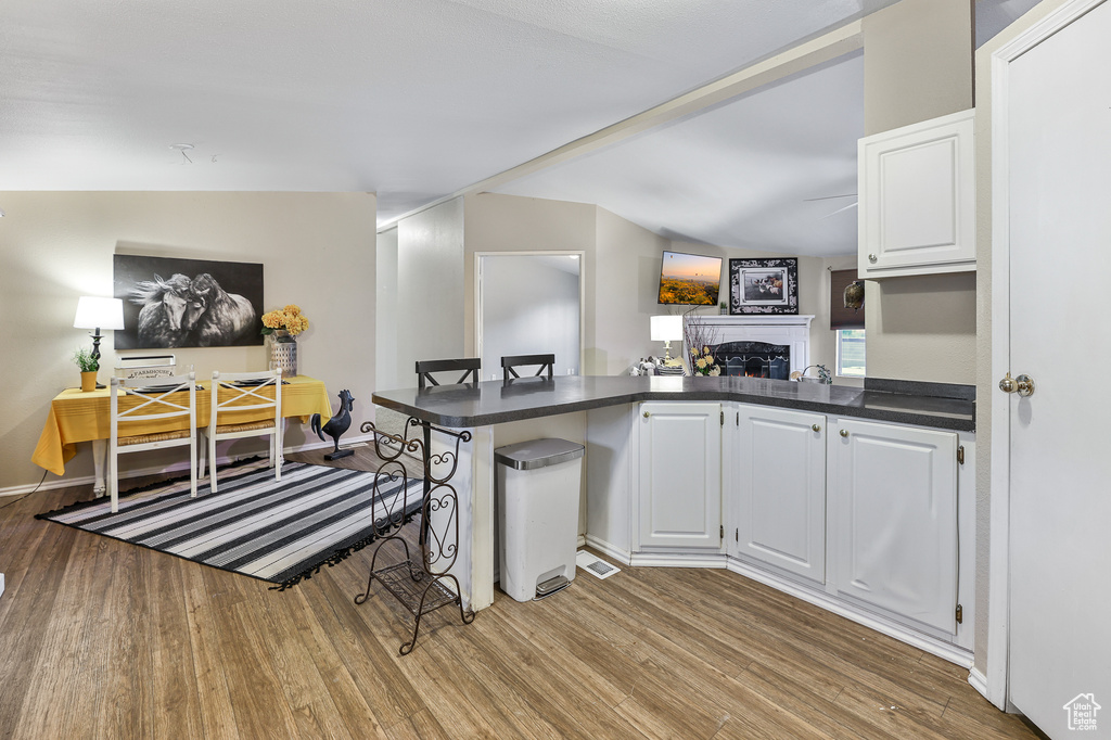 Kitchen with light hardwood / wood-style flooring, white cabinets, a breakfast bar, vaulted ceiling, and kitchen peninsula