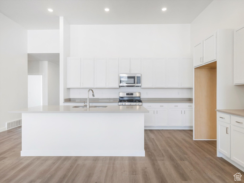 Kitchen with stainless steel appliances, light hardwood / wood-style floors, white cabinets, and a kitchen island with sink