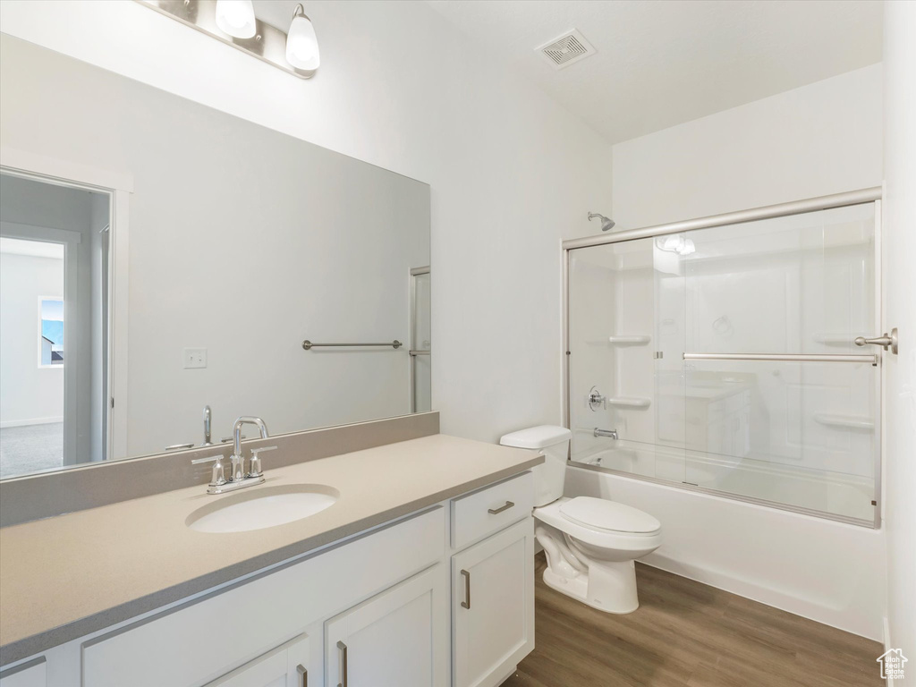 Full bathroom featuring hardwood / wood-style floors, toilet, vanity, and shower / bath combination with glass door