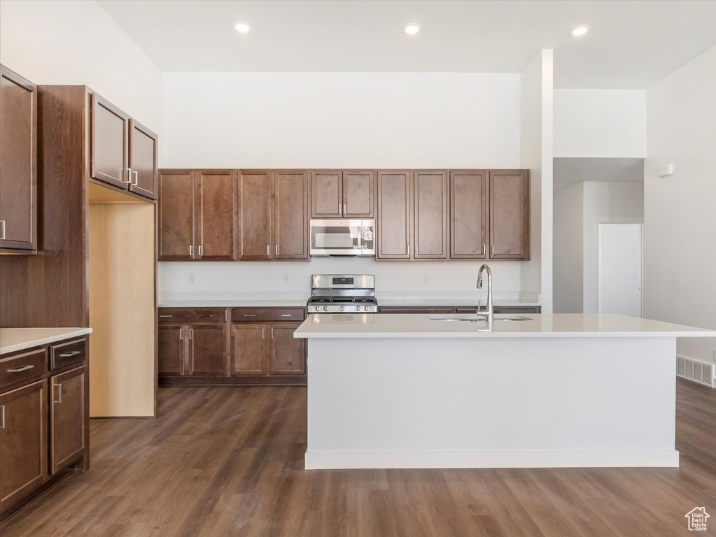 Kitchen featuring a kitchen island with sink, appliances with stainless steel finishes, sink, and dark wood-type flooring