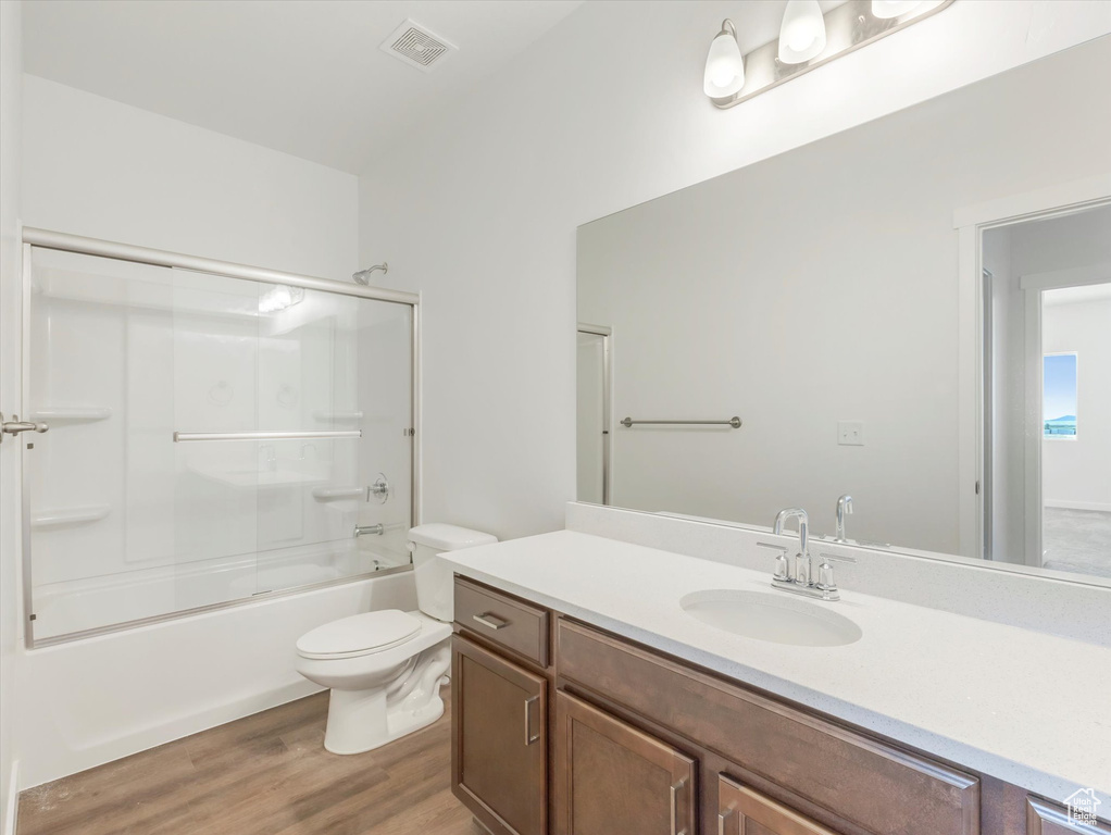 Full bathroom featuring combined bath / shower with glass door, toilet, vanity, and wood-type flooring