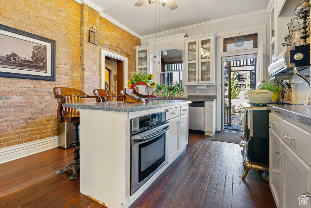 Kitchen with ceiling fan, dark hardwood / wood-style floors, white cabinetry, appliances with stainless steel finishes, and a breakfast bar area