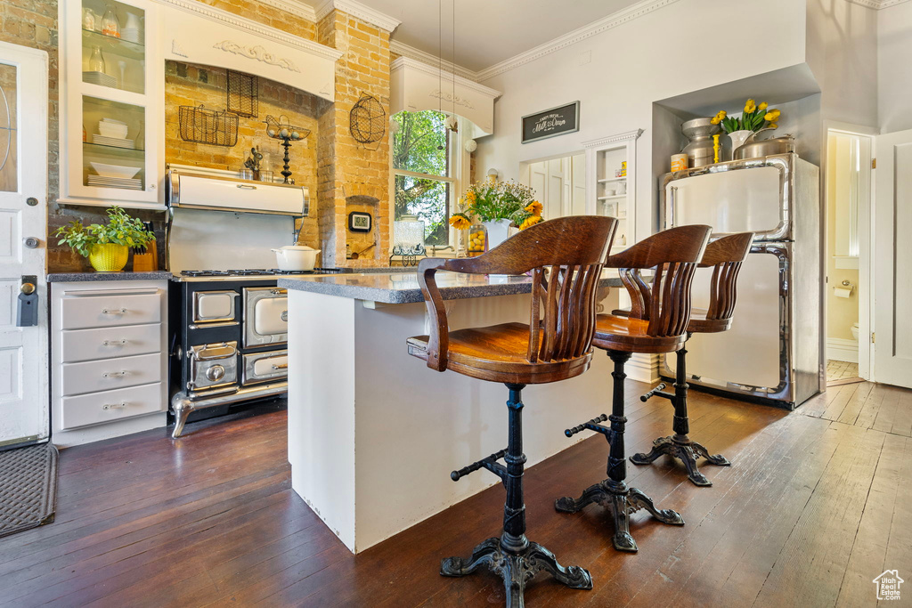 Kitchen with fridge, extractor fan, hardwood / wood-style flooring, a breakfast bar area, and crown molding