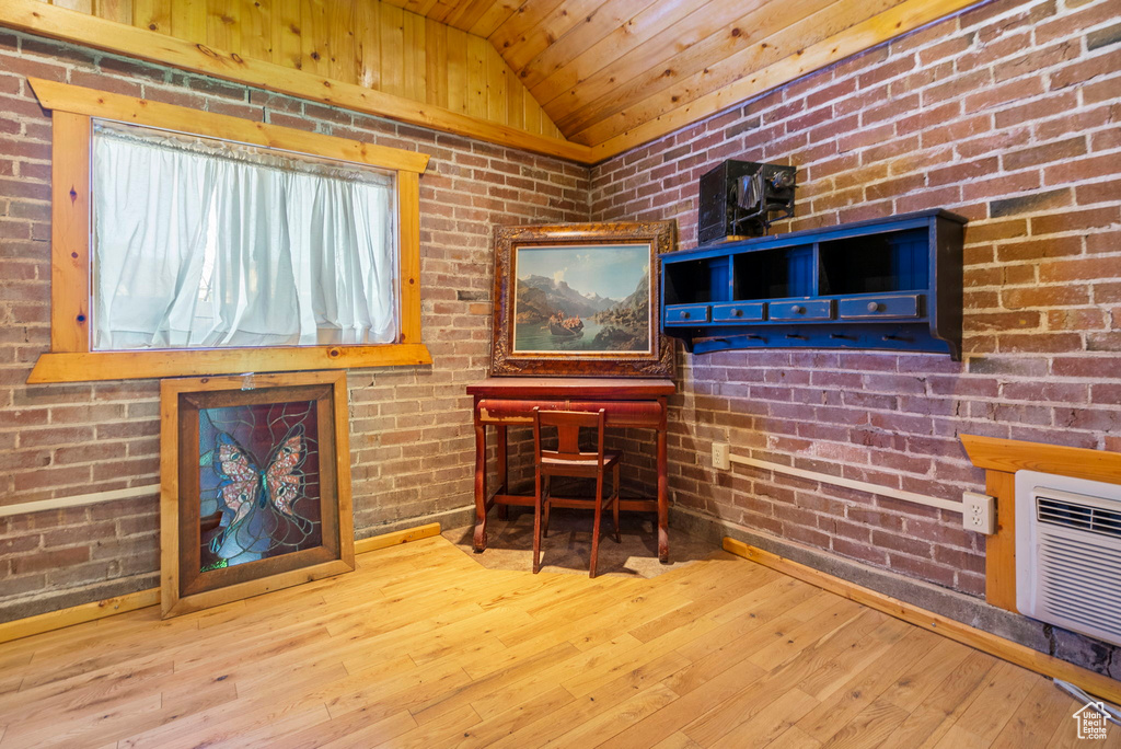 Office space featuring vaulted ceiling, light hardwood / wood-style flooring, and brick wall