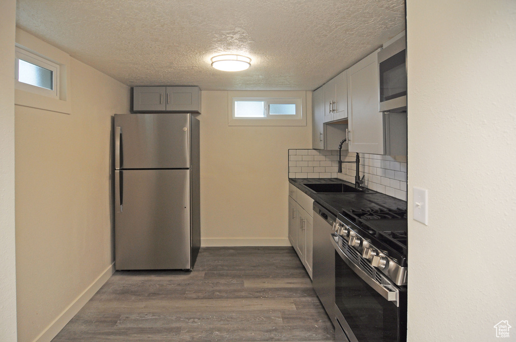 Kitchen featuring stainless steel appliances, tasteful backsplash, sink, a textured ceiling, and dark hardwood / wood-style flooring