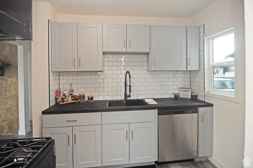 Kitchen with stainless steel dishwasher, tasteful backsplash, sink, stove, and hardwood / wood-style flooring