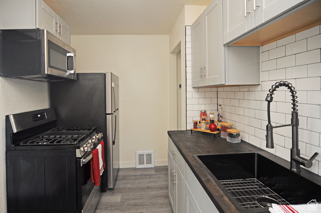 Kitchen with appliances with stainless steel finishes, tasteful backsplash, sink, wood-type flooring, and wooden counters