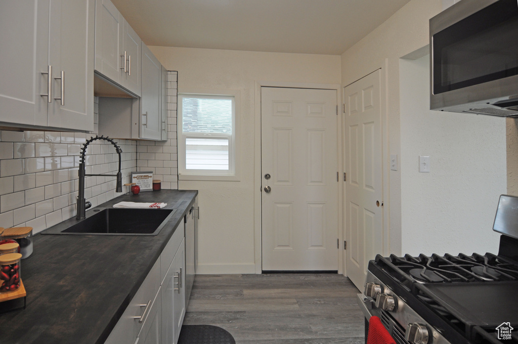 Kitchen featuring sink, appliances with stainless steel finishes, wood-type flooring, tasteful backsplash, and white cabinetry