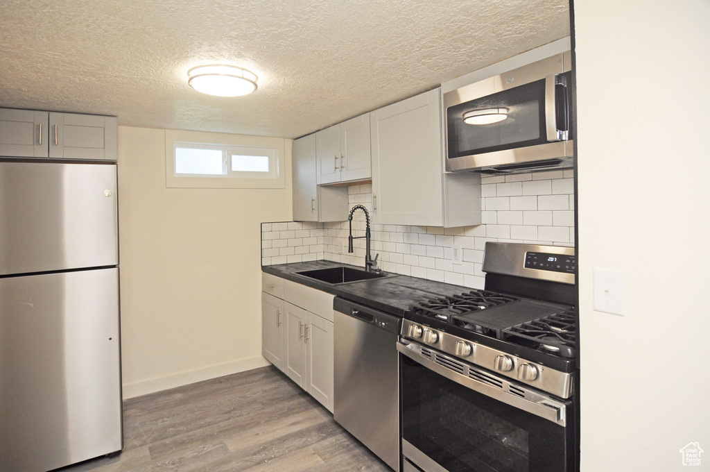 Kitchen with light wood-type flooring, tasteful backsplash, appliances with stainless steel finishes, sink, and a textured ceiling