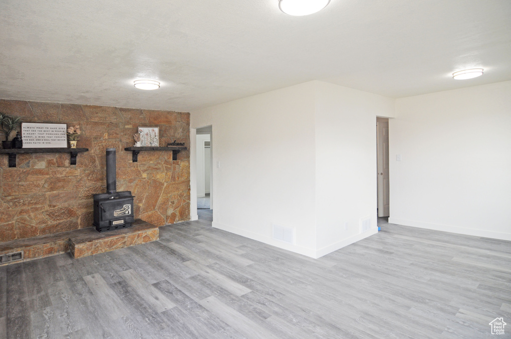 Unfurnished living room featuring light hardwood / wood-style flooring, a wood stove, and tile walls