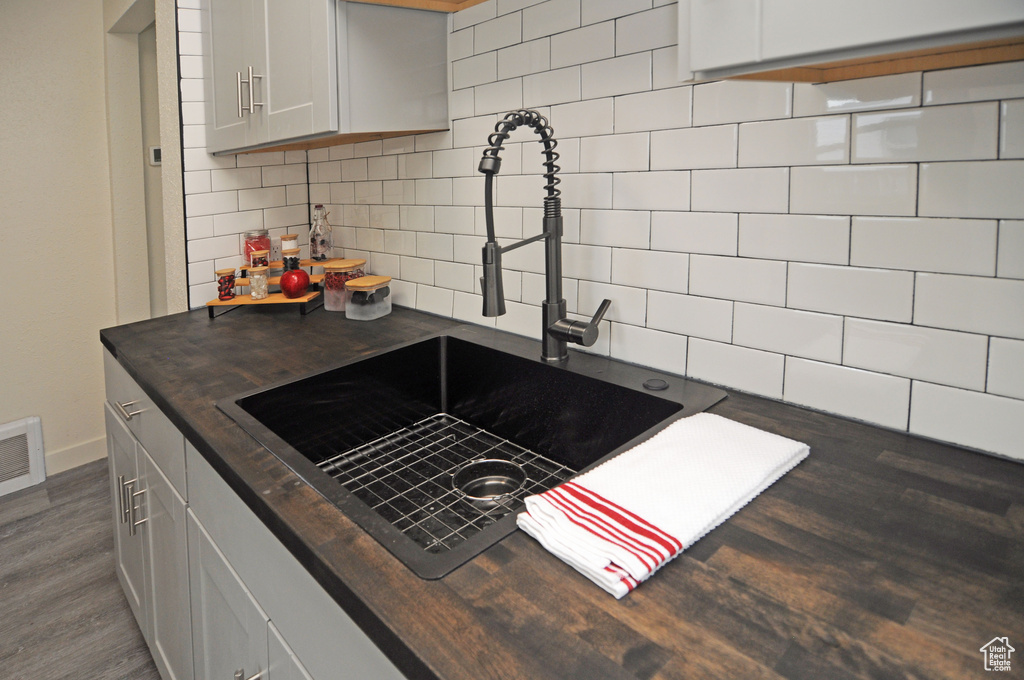 Kitchen featuring wooden counters, sink, dark wood-type flooring, tasteful backsplash, and white cabinetry