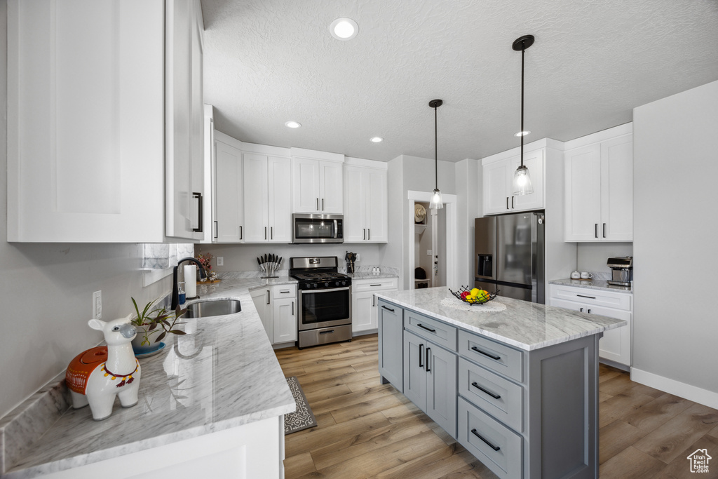 Kitchen with a kitchen island, hanging light fixtures, white cabinetry, sink, and stainless steel appliances