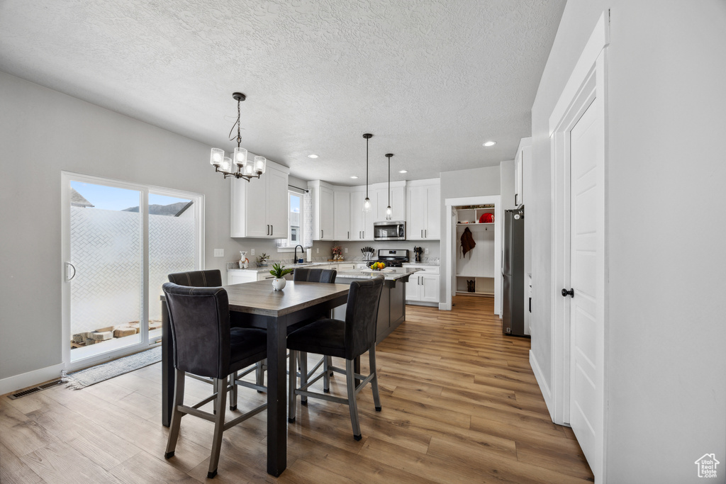 Dining area featuring sink, light hardwood / wood-style flooring, a textured ceiling, and a chandelier