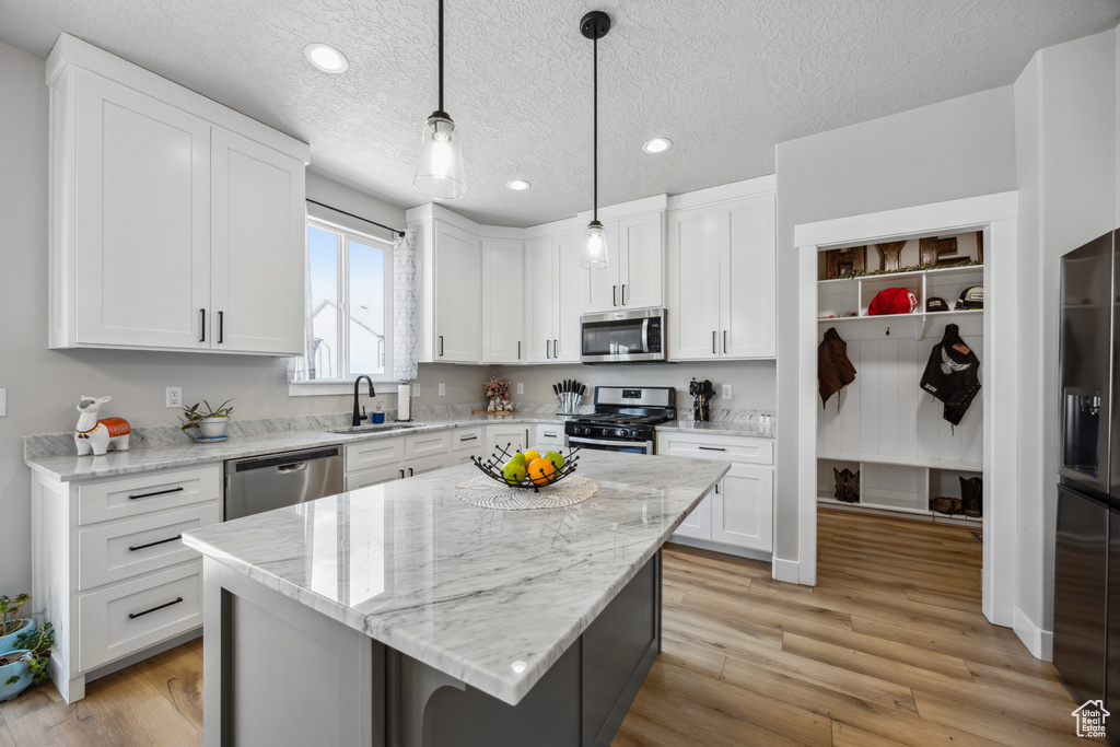Kitchen featuring appliances with stainless steel finishes, light hardwood / wood-style flooring, sink, a center island, and hanging light fixtures